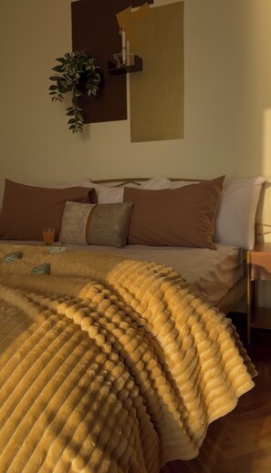 Una cama bien tendida con un edredón texturizado, una mesita de noche con una lámpara y una planta colgada en la pared.