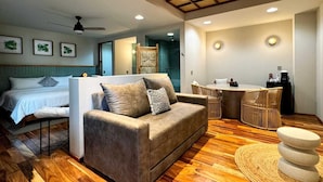 Een moderne hotelkamer met houten vloer, een bank, een bed, een eethoek en een plafondventilator.