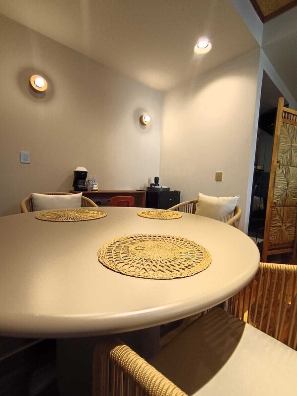 A round dining table with woven placemats, wicker chairs, and a coffee machine on a counter. - MUSA HOTEL BOUTIQUE (Bucerias)