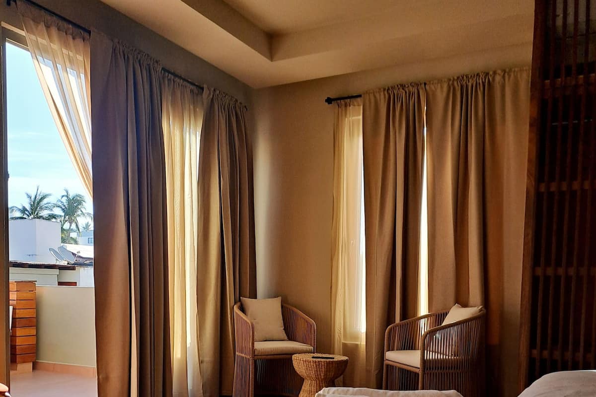 Habitación de hotel con una cama, dos sillas, una mesita y vistas al exterior.