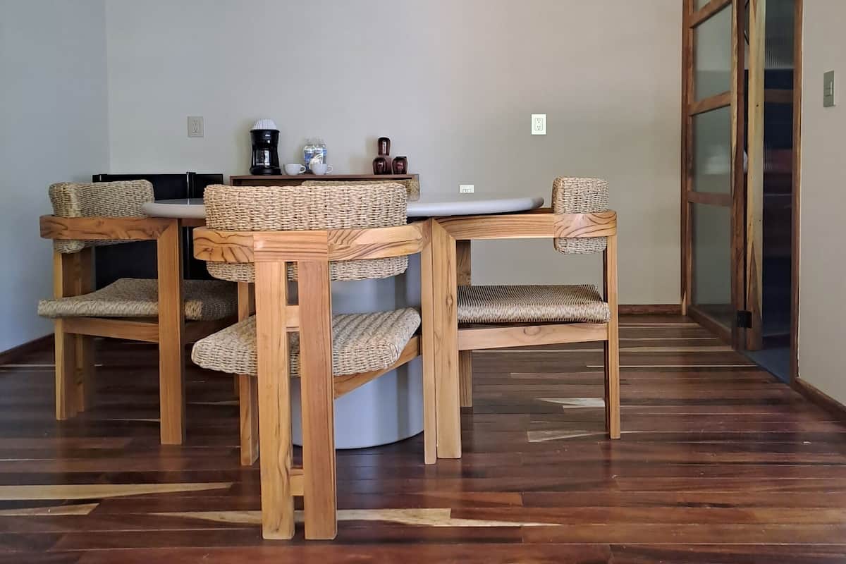 Un comedor con una mesa redonda y cuatro sillas, cada una con asientos y respaldos de mimbre.