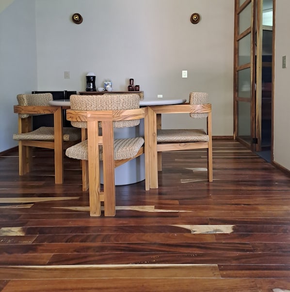 Zona pranzo con tavolo rotondo e quattro sedie, ognuna con seduta e schienale intrecciati.