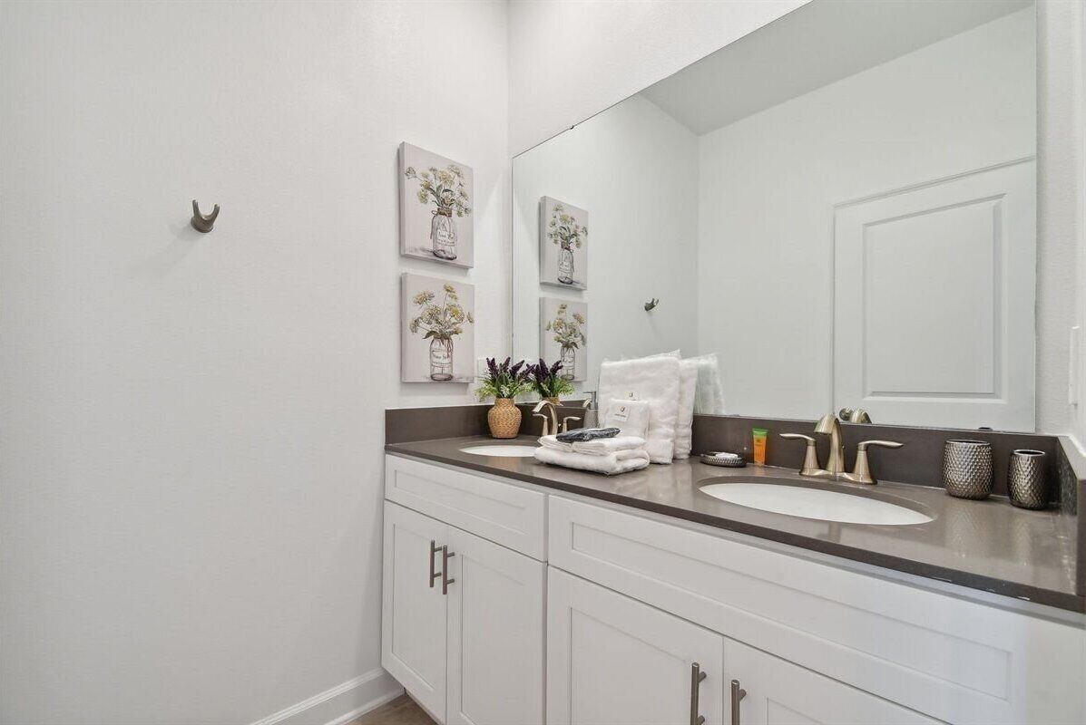 A modern bathroom with a white vanity, a large mirror, and decorative wall art.