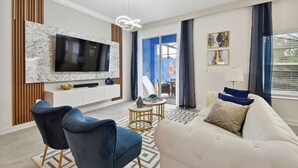 A modern living room with a marble TV wall, a sofa, two chairs, and a small round table. - 5br/4ba Luxury Home Resort Access (Kissimmee)