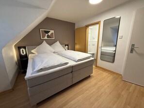 Une chambre à coucher comprenant un lit, une table de chevet, un miroir et une porte donnant sur une salle de bain.