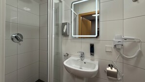 A modern bathroom with a glass shower enclosure, a white sink, a mirror with integrated lighting, and a hairdryer on the wall. - SHIN CENTRAL (Essen)