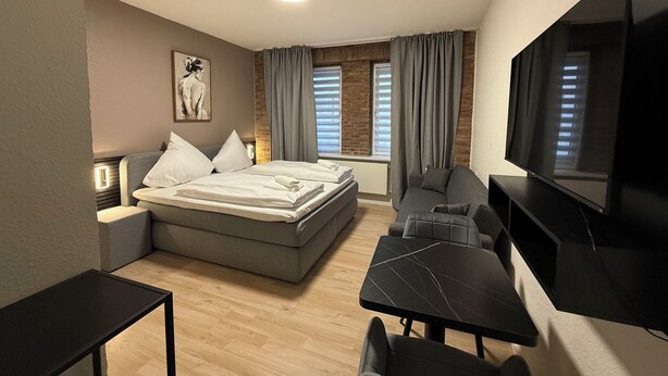 A modern hotel room with a bed, a desk, a chair, a TV, and a large window with curtains. - SHIN CENTRAL (Essen)