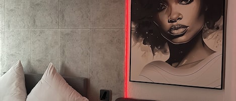 Una habitación moderna con un sofá gris, una cama con almohadas blancas y una obra de arte colgada en la pared.