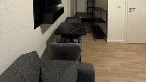 A modern living room with a flat-screen TV mounted on the wall, a sofa, and a dining table with chairs. - SHIN CENTRAL (Essen)