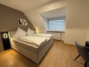 Una camera da letto con un letto, una sedia, un termosifone e una finestra con persiane.