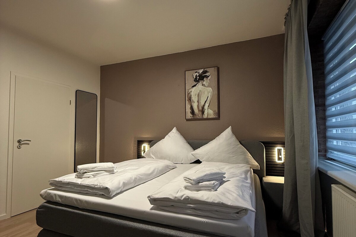 Une chambre à coucher moderne avec un grand lit, des lampes de chevet, un tableau au mur et une fenêtre avec des stores.