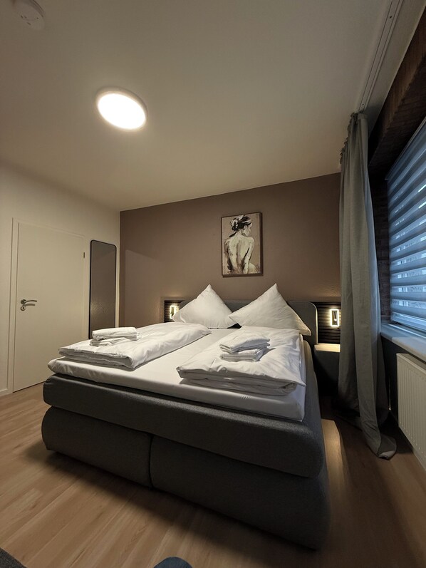 Una camera da letto moderna con un letto grande, lampade sui comodini, un quadro al muro e una finestra con persiane.