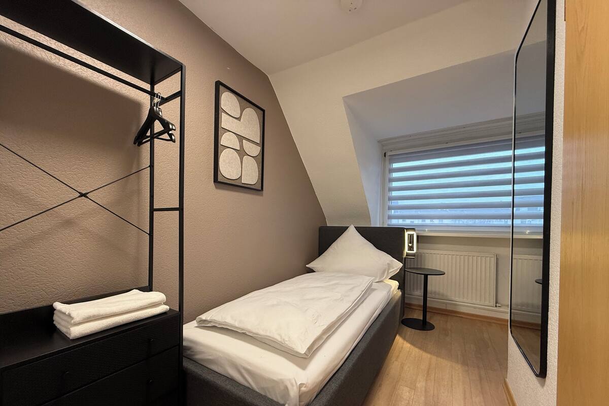 A bedroom with a bed, a dresser, a mirror, and a window with blinds.