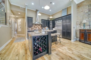 A modern kitchen with a central island, dark cabinetry, and a brick accent wall.