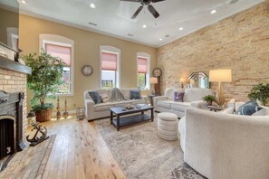 A living room with a fireplace, a ceiling fan, and a brick wall.