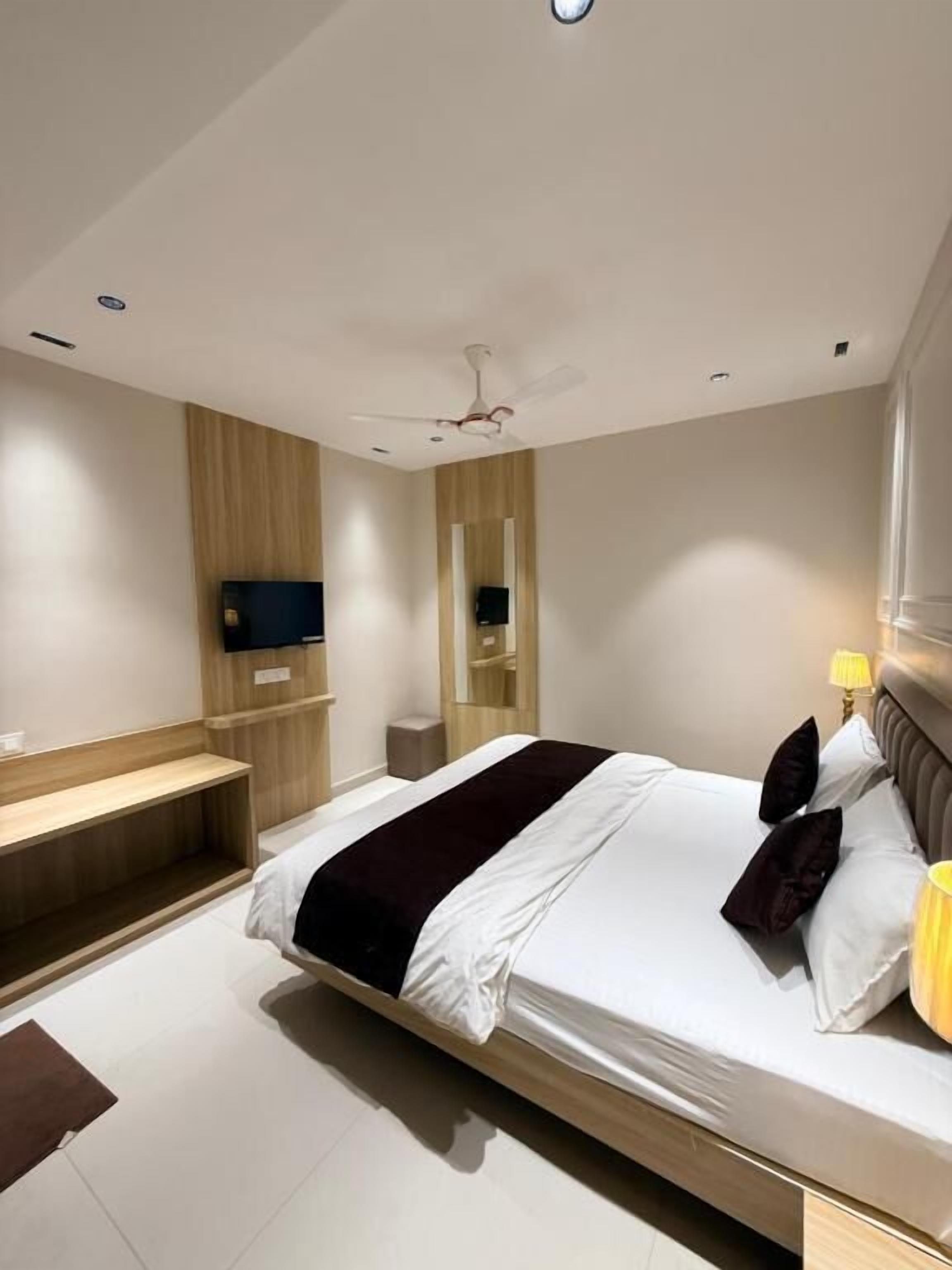 Una camera d'albergo moderna con un letto grande, una TV a schermo piatto fissata al muro, un comodino e una ventola a soffitto.