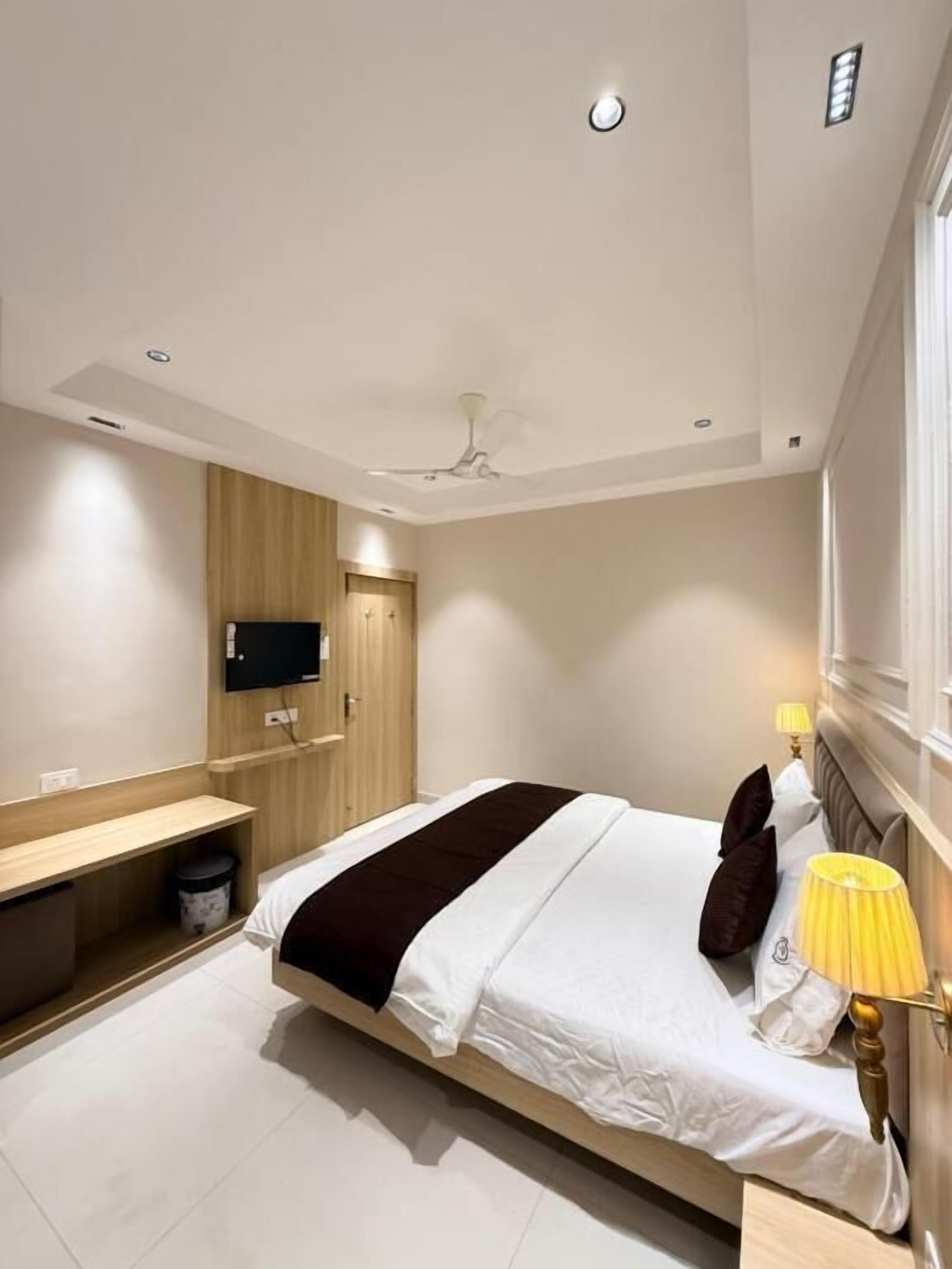 A modern hotel room with a bed, bedside table, lamp, TV, and a ceiling fan.