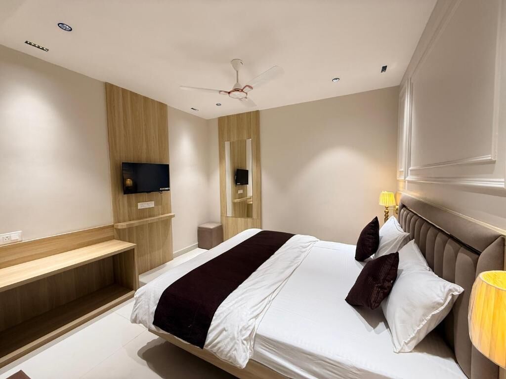 A modern hotel room with a large bed, a TV mounted on the wall, a ceiling fan, and a bedside table with a lamp.