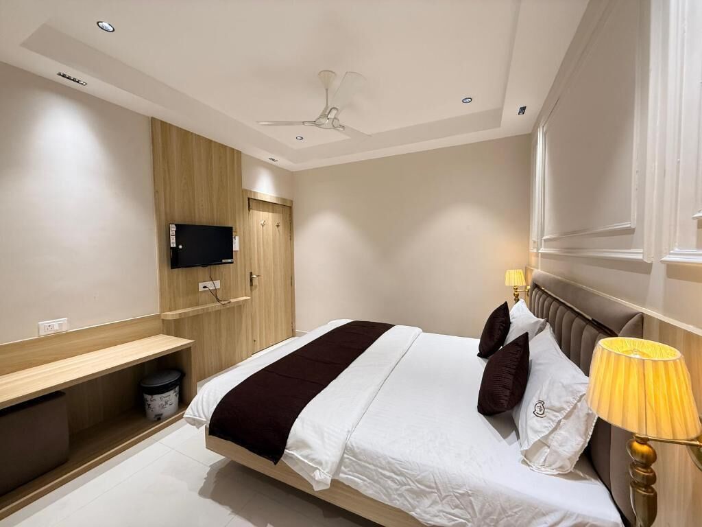 Ein modernes Hotelzimmer mit einem Bett, einem an der Wand befestigten Fernseher, einem Deckenventilator und einer Nachttischlampe.