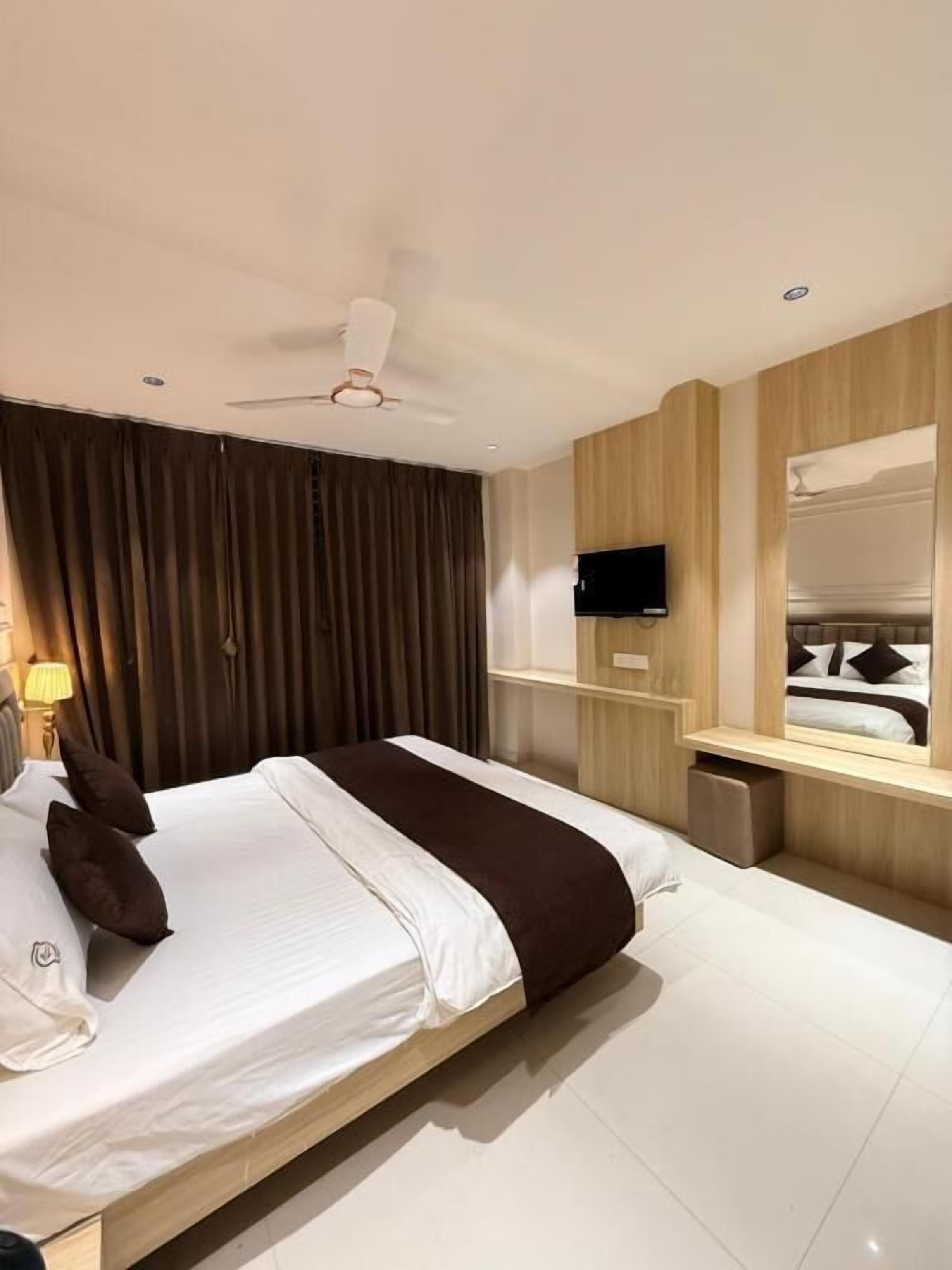 A modern hotel room with a large bed, a ceiling fan, a TV mounted on the wall, and a mirror above the bed.