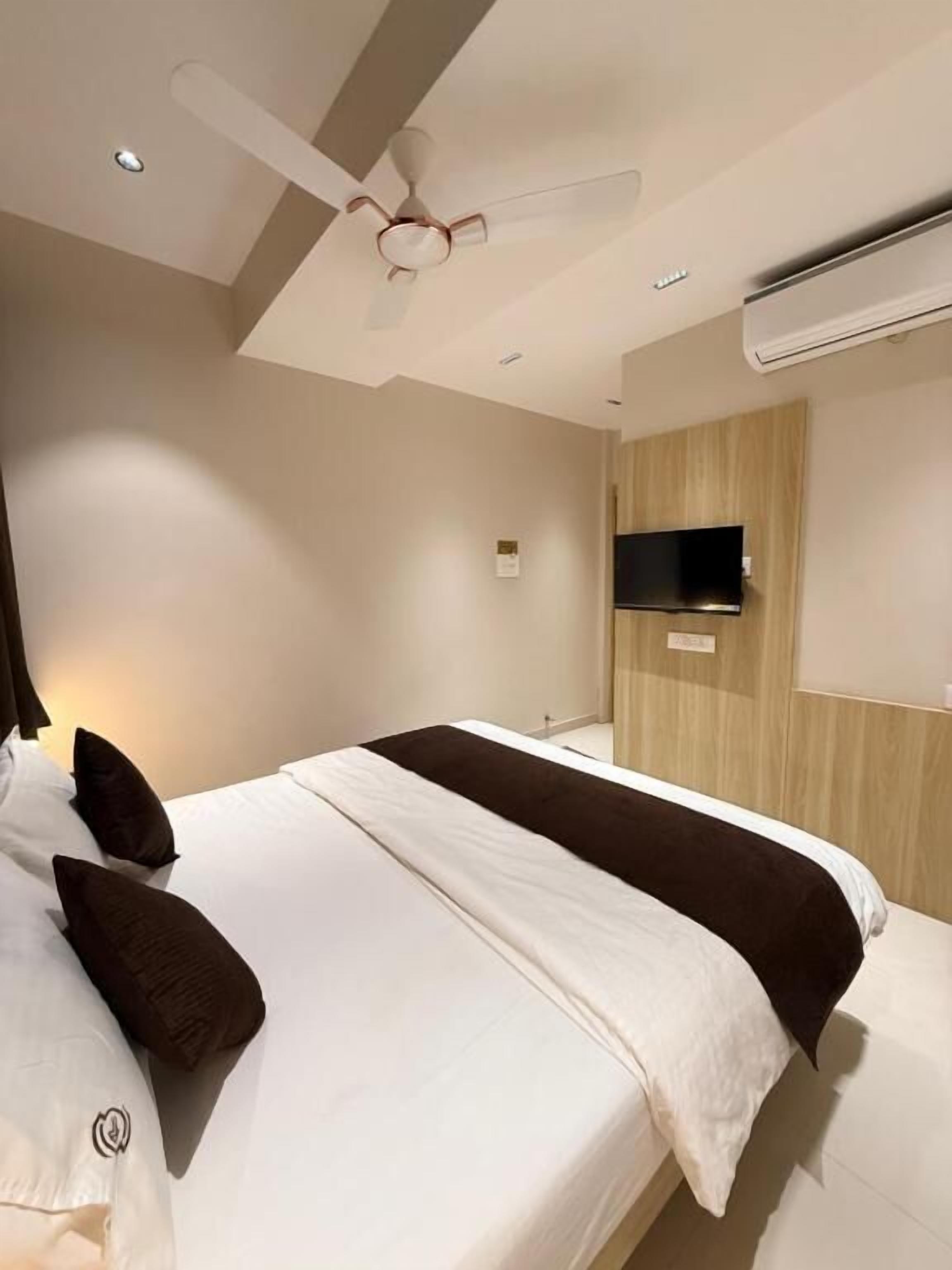 A modern hotel room with a large bed, a ceiling fan, an air conditioning unit, and a flat-screen TV mounted on the wall.