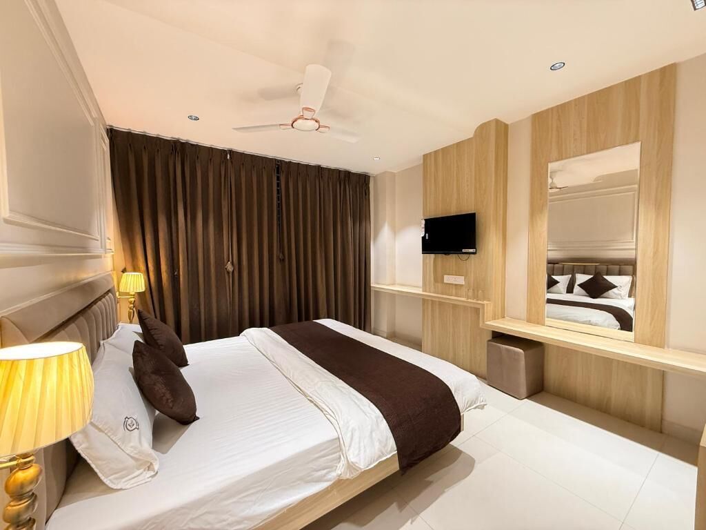 Une chambre d’hôtel avec un lit, un téléviseur fixé au mur, un ventilateur de plafond et une fenêtre avec des rideaux.