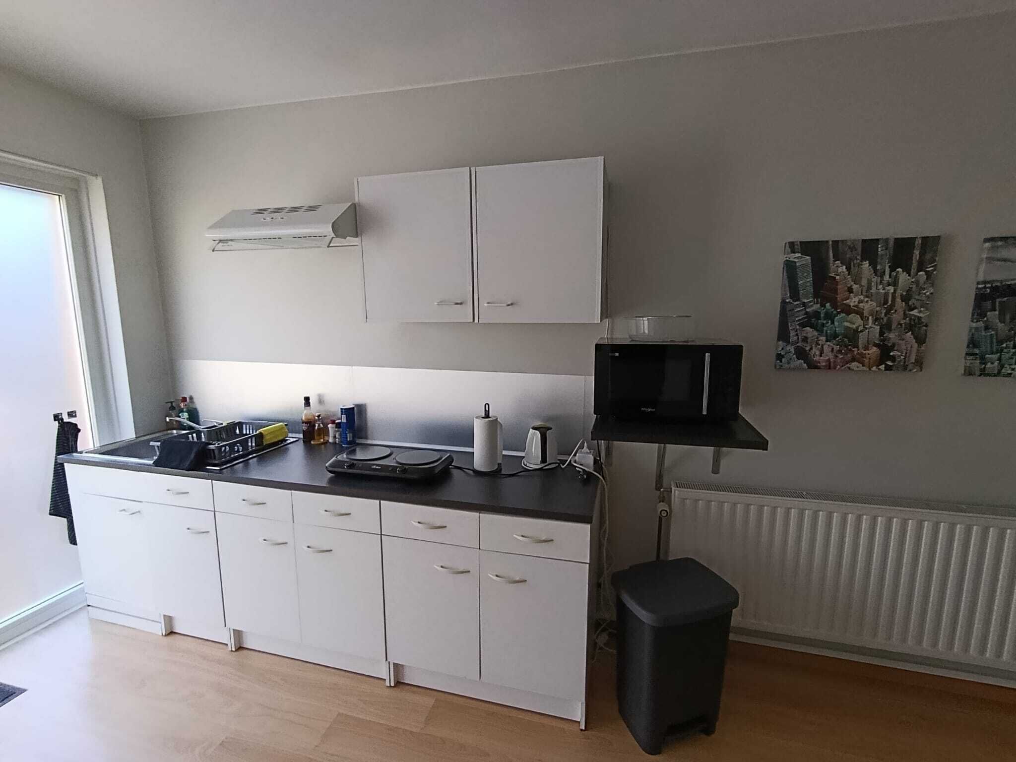 Ett modernt kök med vita skåp, en mikrovågsugn och en liten svart papperskorg.