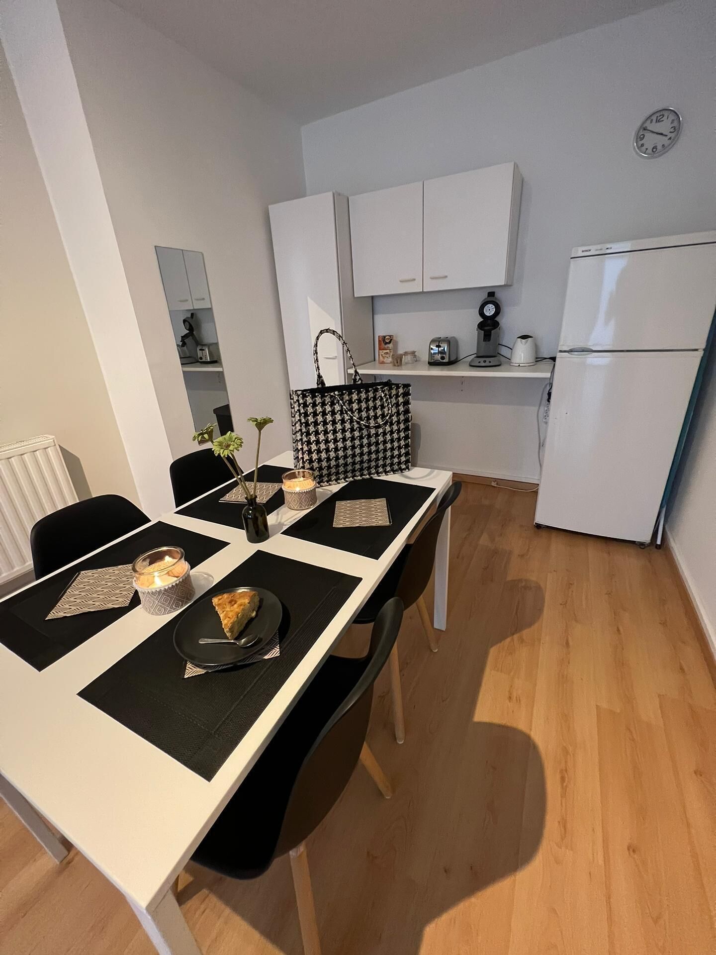 A compact kitchen with white cabinets, a refrigerator, and a dining table set with placemats and a candle.