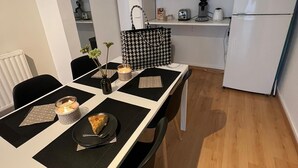 Kompakti keittiö, jossa on valkoiset kaapit, jääkaappi ja ruokapöytä, jonka päällä on alustat ja kynttilä.