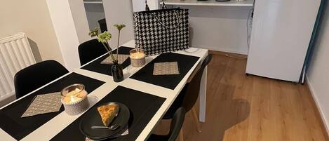 A compact kitchen with white cabinets, a refrigerator, and a dining table set with placemats and a candle.