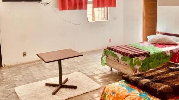 A bedroom with a bed, a small table, a TV mounted on the wall, and a window with red curtains. - Hotel Cetro (Belo Horizonte)