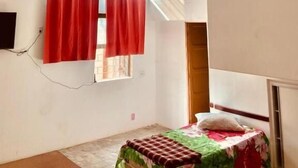 A room with a bed, a ceiling fan, a window with red curtains, and a small table. - Hotel Cetro (Belo Horizonte)