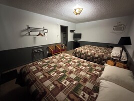 Quarto de hotel com duas camas, uma escrivaninha, uma cadeira, televisão e luminária suspensa.
