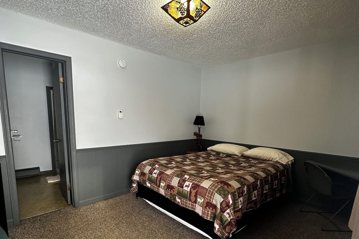 Un dormitorio con cama, mesita de noche, lámpara y puerta.