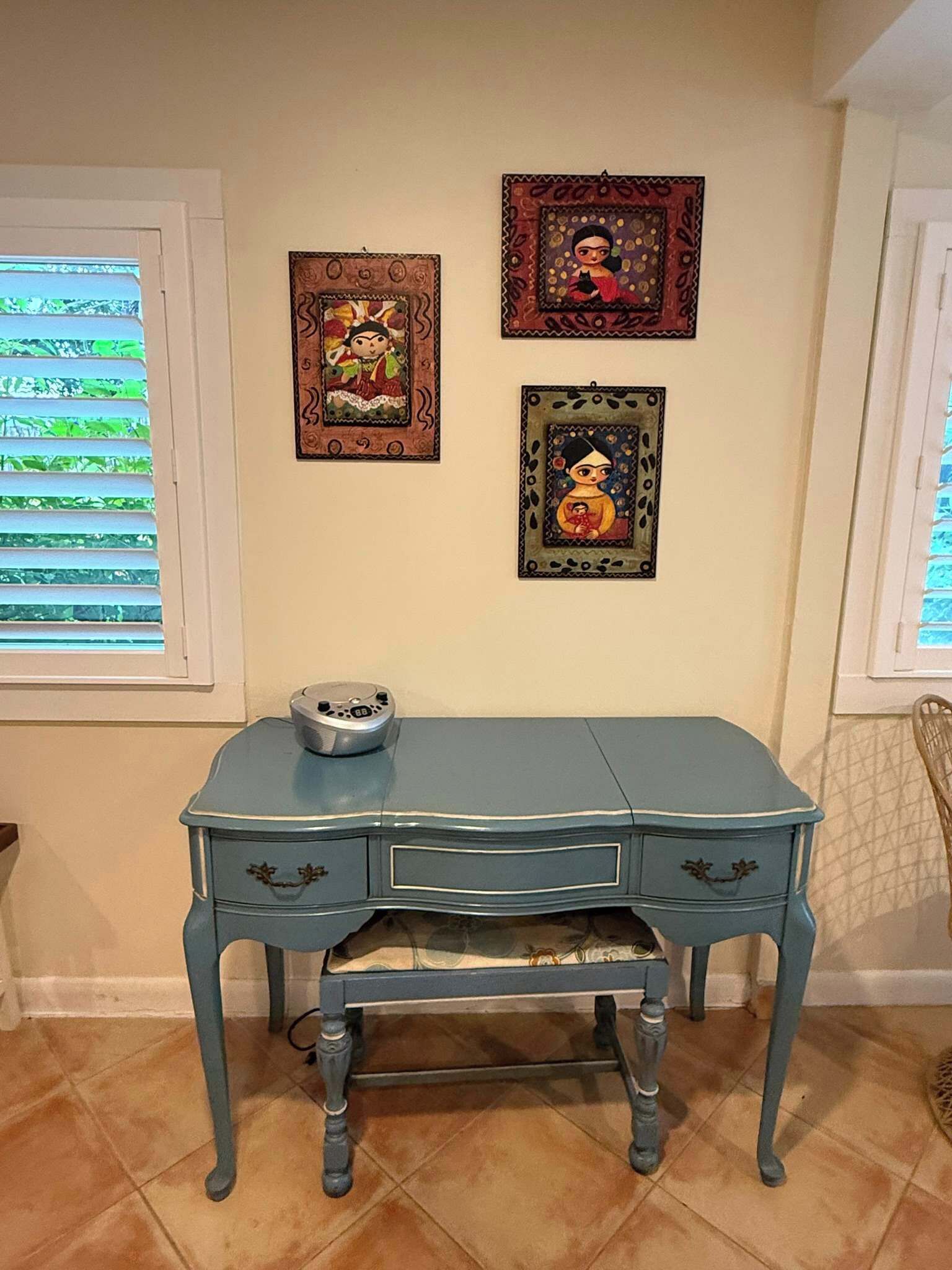 A blue desk with drawers, a radio, and three framed artworks on the wall.