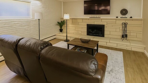 A living room with a brown leather sofa, a flat-screen TV mounted above a fireplace, and a floor lamp. - Romantic Nest-Enjoyable 1-bedroom bungalow in charming Colorado Springs (Colorado Springs)