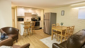 A compact kitchen with white cabinets, a stainless steel refrigerator, a microwave, and a dining area with wooden chairs and a table. - Romantic Nest-Enjoyable 1-bedroom bungalow in charming Colorado Springs (Colorado Springs)