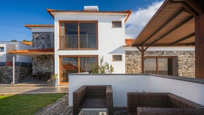 Uma casa moderna de dois andares com fachada de pedra, uma varanda e móveis de vime para área externa.