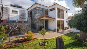 Uma casa moderna de dois andares com fachada de pedra, varanda e um jardim bem cuidado.