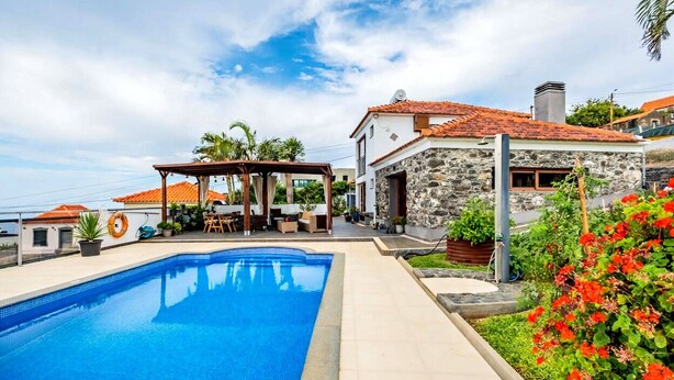Uma piscina, área de estar externa, uma casa de pedra e vista para o mar.