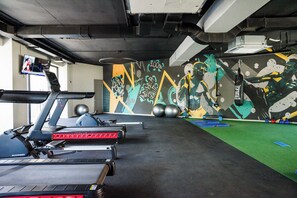 Ett gym med löpband, träningsbollar och en färgstark väggmålning.