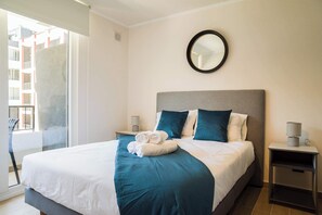 Ett hotellrum med en stor säng, en rund spegel på väggen och utsikt över en byggnad utanför.