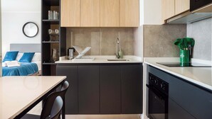 Cocina compacta con armarios oscuros, encimera blanca y lavavajillas. Cuenta con un pequeño comedor con mesa y sillas.