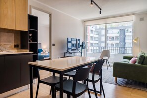 A modern kitchen with a dining area, a TV, and a view of the city through large windows. - Bright 2BR Apartment in Providencia | Ideal For 5 (Providencia)