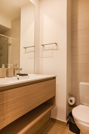 A modern bathroom with a wooden vanity, a large mirror, a toilet, and a trash bin. - Bright 2BR Apartment in Providencia | Ideal For 5 (Providencia)