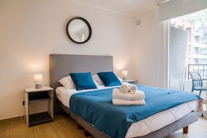 A hotel room with a bed, two bedside tables, a mirror, and a view of the outside. - Bright 2BR Apartment in Providencia | Ideal For 5 (Providencia)