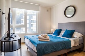 A hotel room with a bed, a TV, a window, and a mirror. - Bright 2BR Apartment in Providencia | Ideal For 5 (Providencia)