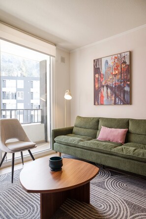 A modern living room with a green sofa, a wooden coffee table, a chair, and a painting on the wall. - Bright 2BR Apartment in Providencia | Ideal For 5 (Providencia)