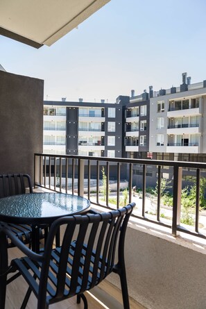 Un balcón con una mesa redonda y sillas, con vistas a un edificio de apartamentos moderno que tiene varios balcones.