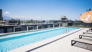 Une piscine sur le toit offrant une vue dégagée sur les gratte-ciel de la ville et les montagnes en arrière-plan.